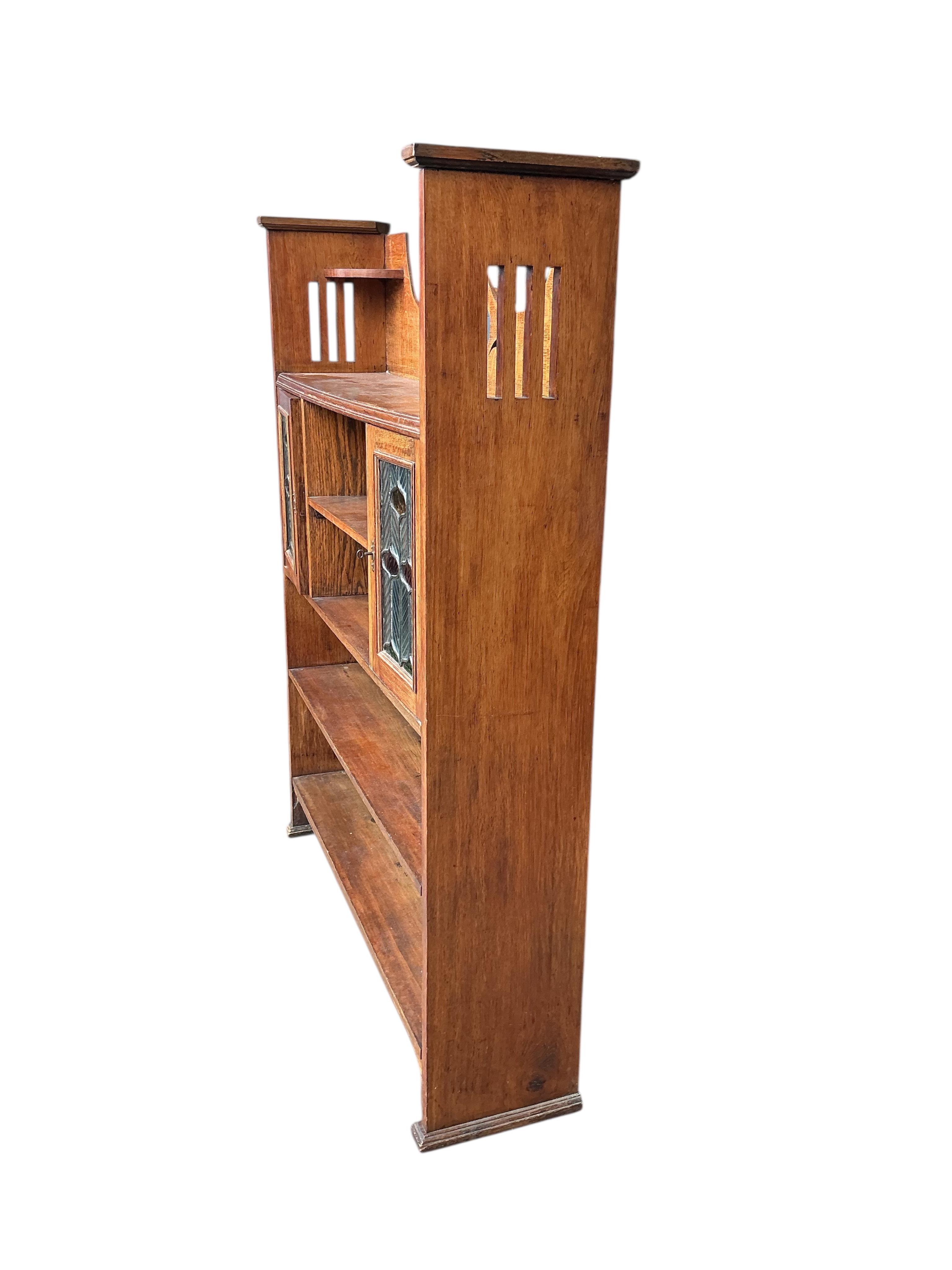 An Arts & Crafts oak open bookcase with stained leaded glass doors, width 108cm, depth 24cm, height 137cm